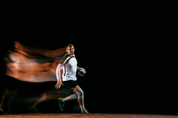 Fototapeta na wymiar Caucasian young handball player in action and motion in mixed lights over black studio background. Fit male professional sportsman. Concept of sport, movement, energy, dynamic, healthy lifestyle.