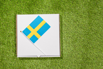Paper box of pizza with Swedish Flag on the grass. Concept. Top view