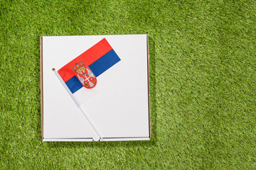 Paper box of pizza with Serbian Flag on the grass. Concept. Top view