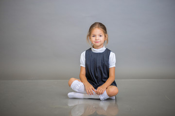 The girl the first grader in a school uniform - a gray sundress and a white blouse poses on a gray background - obrazy, fototapety, plakaty