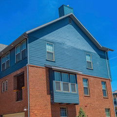Fototapeta premium Square Exterior of homes with wooden and red brick wall against blue sky on sunny day
