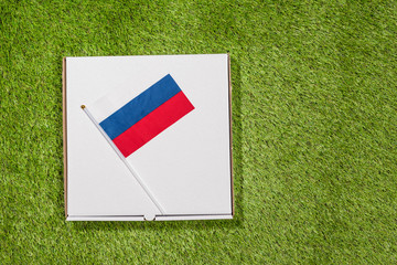 Paper box of pizza with Russian Flag on the grass. Concept. Top view