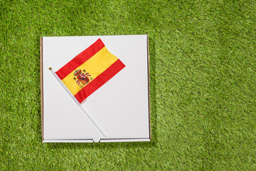 Paper box of pizza with Spanish Flag on the grass. Concept. Top view