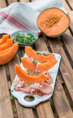 Plate with melon and jamon, wooden table, snack