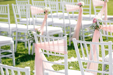 White chairs for a wedding ceremony outdoors in the summer, decorated with delicate light pink ribbons and fresh flowers