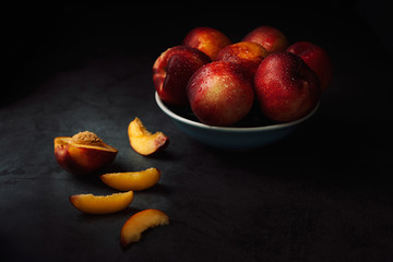 Fototapeta na wymiar Still life of fresh nectarines with droplets of water in a bowl on dark background. Low key.