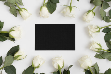 Top view of a black card mockup with roses on a white table.