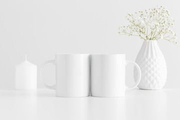 Two mugs mockup with a candle and a gypsophila on a white table.