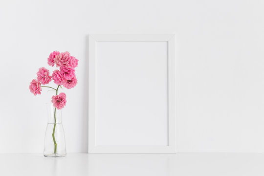 White frame mockup with pink roses in a glass vase on a white table.Portrait orientation.