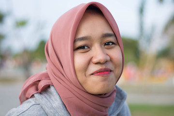 portrait of Muslim young women wearing hijabs who happily pose in front of cameras in city parks. Women see a camera with trees in the background.