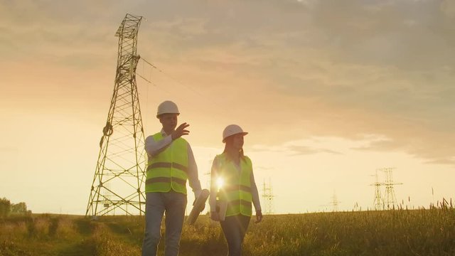 Coworking engineers with tablets on solar plant. Adult men and women in hardhats using tablets while standing outdoors on transformer platform. Transportation of clean energy