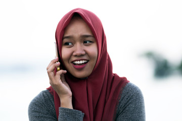 close up shot of a hijab woman sitting on the sidewalk in the beautiful sunshine of a mangrove garden while calling her handphone