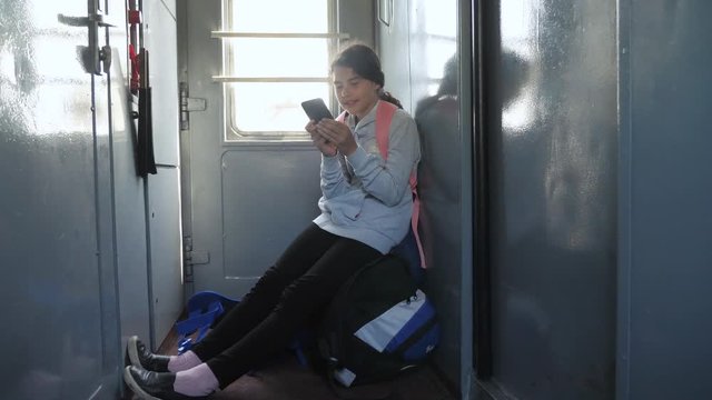 Teenager girl traveler with a backpack sitting on bags backpacks at the window of the car with a smartphone. Travel rail carriage concept. the girl in the train at the window corresponds to the girl