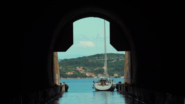 Beautiful shoot from the inside of the submarine bunker. A white sailboat is parked outside on a sunny summer day. Travel holiday destination. 