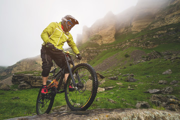 Fototapeta premium Side view wide angle partly a man on a mountain bike travels on rocky terrain Against the background of cloudy sky and epic rocks. The concept of a mountain bike and mtb downhill