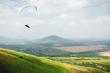 Fototapeta na wymiar A paraglider flies in the sky in a cocoon suit on a paraglider over the Caucasian countryside with hills and mountains. Paragliding Sport Concept