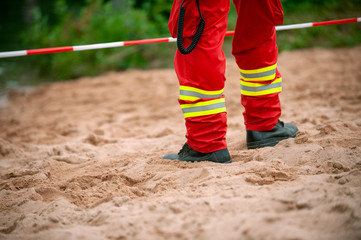 Plakat Legs of Rescuer standind on the Sand in front of red and white tape.