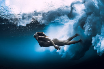 Woman swim underwater with big ocean wave.