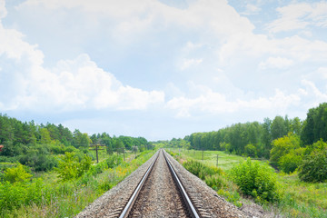 A railway through the summer green fields.  Beautiful green railway tree landscape sky with clouds. Beautiful landscape. Railway transport.
