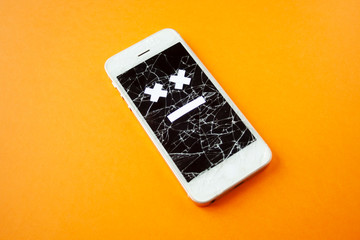Broken smartphone with cracked destroyed screen on orange background with sad smile. Broken phone...