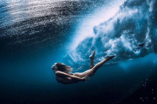 Woman swim underwater with ocean wave.