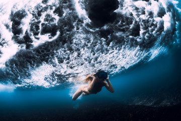 Young woman swim underwater with ocean wave.