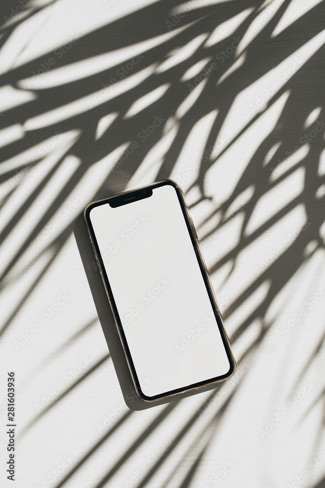 Wall mural smart phone with copy space mock up screen on white background with palm leaves shadow. flat lay, to