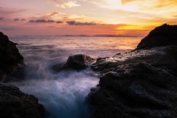 Fototapeta na wymiar long exposure of motion ocean wave crashing on the rocks in sunset background