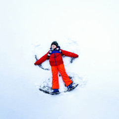 Cute little kid boy in colorful winter clothes making snow angel, laying down on snow. Active outdoors leisure with children in winter. Happy child having fun and laughing.