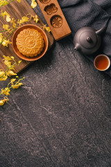 Mid-Autumn Festival traditional food concept - Beautiful Moon cake on black slate table with tea, pastry mold, flower, top view, flat lay, copy space
