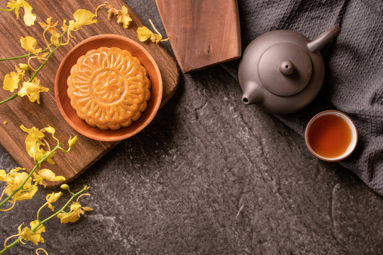 Mid-Autumn Festival traditional food concept - Beautiful Moon cake on black slate table with tea, pastry mold, flower, top view, flat lay, copy space