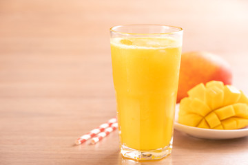 Fresh mango juice with beautiful chopped pulp flesh and straw on bright wooden table background. Tropical fruit design concept. Close up, copy space.