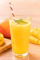 Fresh mango juice with beautiful chopped pulp flesh and straw on bright wooden table background. Tropical fruit design concept. Close up, copy space.