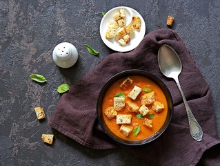 Pumpkin, carrot and tomato puree soup in a black bowl on a dark concrete background. Served with croutons. Thanksgiving day concept. American cuisine. Autumn harvest. Top view