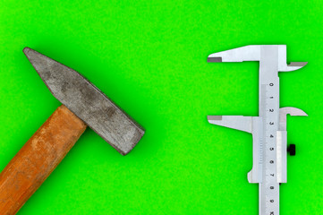 caliper and hammer on green background close-up top view
