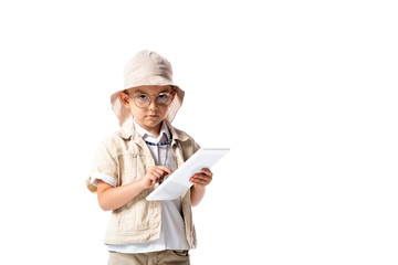 serious explorer child in glasses and hat holding digital tablet and looking at camera isolated on white