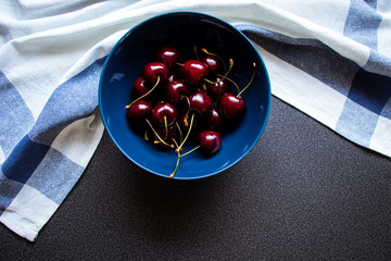 Cherries in a ceramic bowl on a dark background and kitchen towel with a line. Top view.