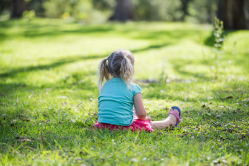 Fototapeta na wymiar little girl sitting on grass in the park with her back turned