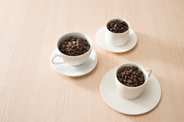 Full coffee beans cups on the wood background