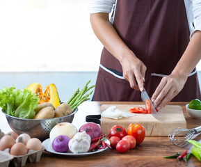 Close-up. The cook's hand is slicing vegetables. on a wooden chopping board with a knife on the kitchen table filled with vegetables
