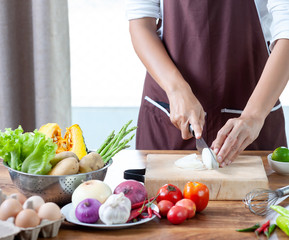 Close-up. The cook's hand is slicing vegetables. on a wooden chopping board with a knife on the kitchen table filled with vegetables