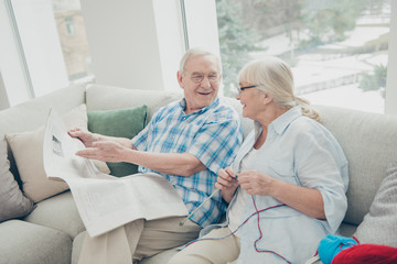 Fototapeta premium Portrait of his he her she two nice cheerful cheery people life partners sitting on divan reading world news paper knitting clothing in light white interior living-room house