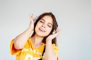 Happy carefree smiling teenager girl with dark long hair in yellow t-shirt listening music in headphones isolated on grey background