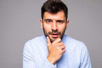 Obraz premium Young handsome man with hand on chin thinking about question, pensive expression over isolated gray background. Smiling with thoughtful face. Doubt concept.