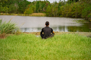 Obraz na płótnie Canvas A man sits on the ground in meditation overlooking a beautiful lake in Orlando, Florida.