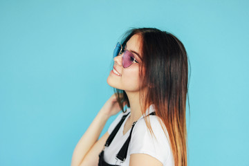 Beautiful happy girl in heart shape sunglasses with dark long hair in white t-shirt isolated on blue background