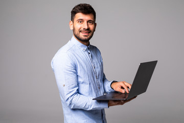 Confident young man holding laptop and typing while standing against grey background