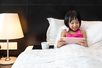 Asian Little Chinese Girl playing tablet in bed