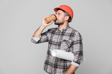 Smiling engineer in safety hemlet holding blueprints and coffee to go isolated on white background