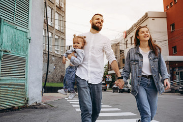 concept of a young happy family with one child: parents carry their baby in their arms while walking around the evening city in the middle of the buildings
